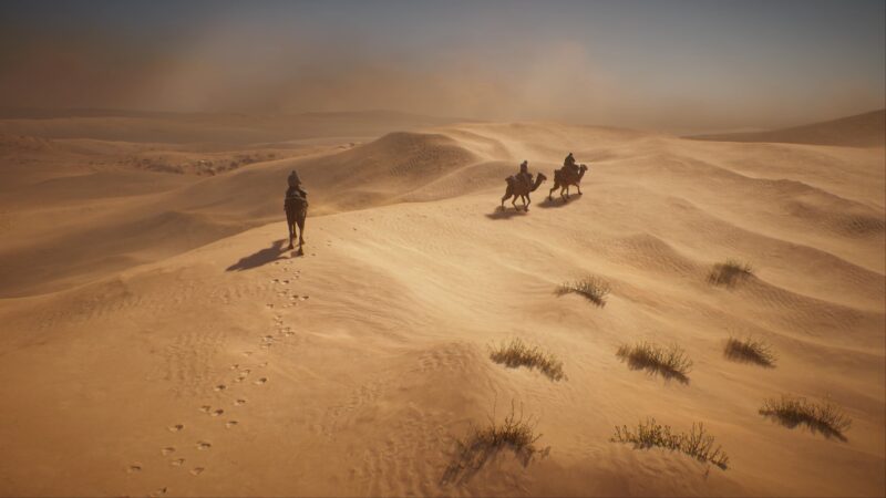 Three riders traverse a vast, sandy desert landscape, leaving footprints behind, with gently rolling dunes and a hazy sky in the background.