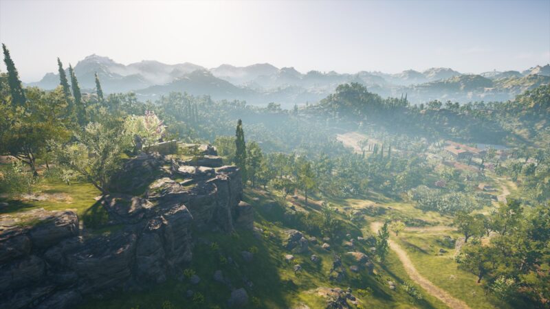 A panoramic view of a sunlit landscape featuring green hills, distant mountains, and a winding path, dotted with trees and rocky outcrops under a clear blue sky.