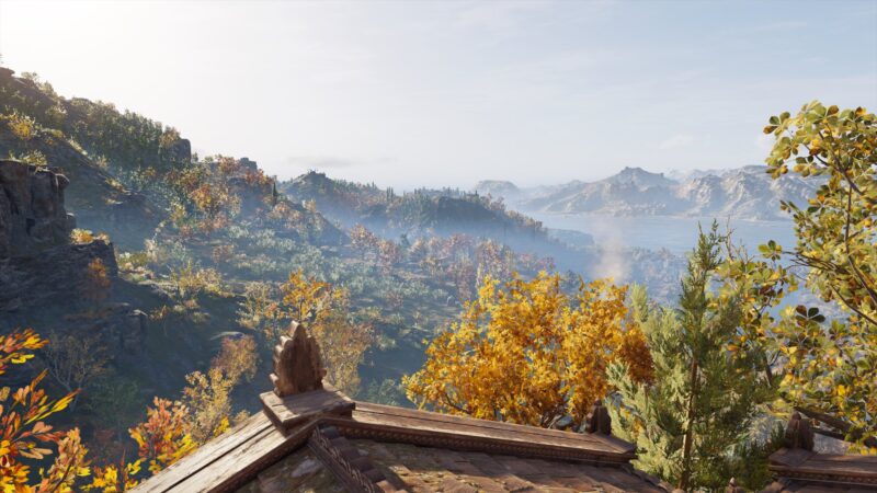 A panoramic view of a misty landscape features vibrant autumn foliage and distant mountains, illuminated by bright sunlight, with the gentle slopes of a roof in the foreground.