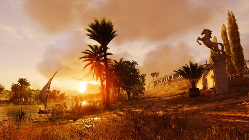 A vibrant sunset casts golden hues over a sandy landscape, with palm trees, a statue of a horse, and a tranquil river with a traditional sailboat.