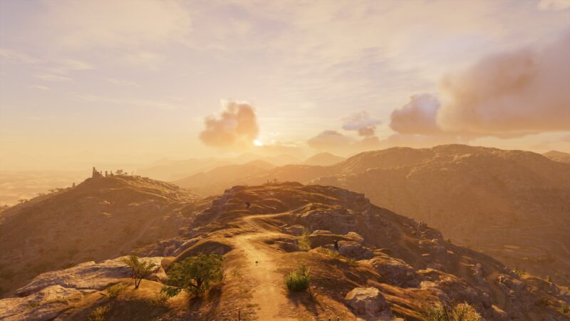 A vast, sunlit landscape shows rolling hills with rocky outcrops and sparse vegetation, as the sun sets behind distant mountains, casting warm, golden light across the scene.