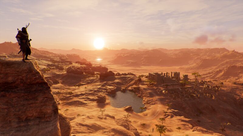 A silhouetted figure stands atop a rocky ledge, overlooking a vast desert landscape with a shimmering lake and ruins, illuminated by the warm glow of a setting sun.