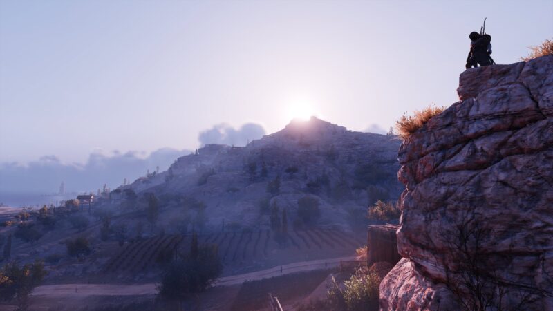 A silhouetted figure stands atop a rocky outcrop, overlooking a vast landscape of rolling hills, vineyards, and a rising sun illuminating the misty scene.