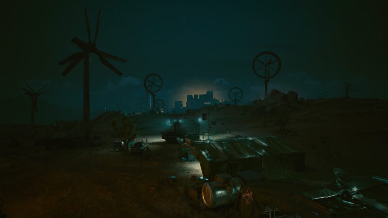 A dark, dystopian landscape features wind turbines illuminated by faint city lights, with makeshift shelters and scattered debris under a night sky filled with clouds.