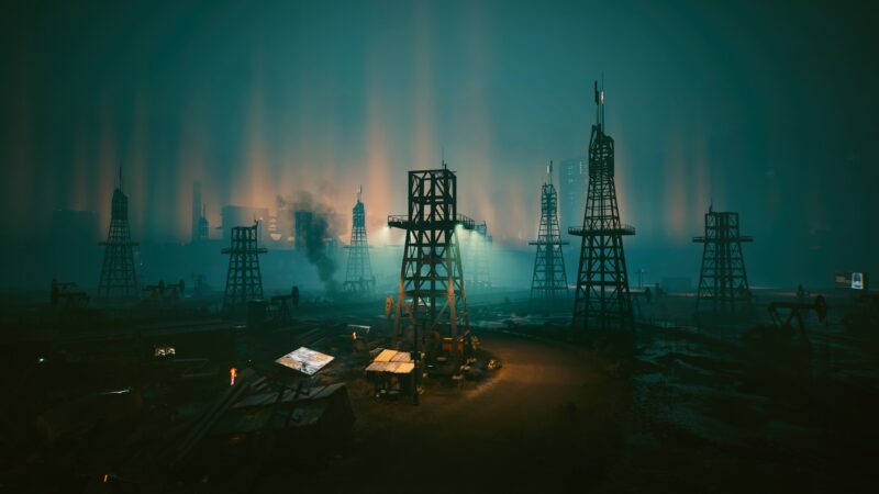 A foggy, industrial landscape features silhouetted oil rigs against a backdrop of vibrant, diffused lights, creating a moody, neon-lit atmosphere.