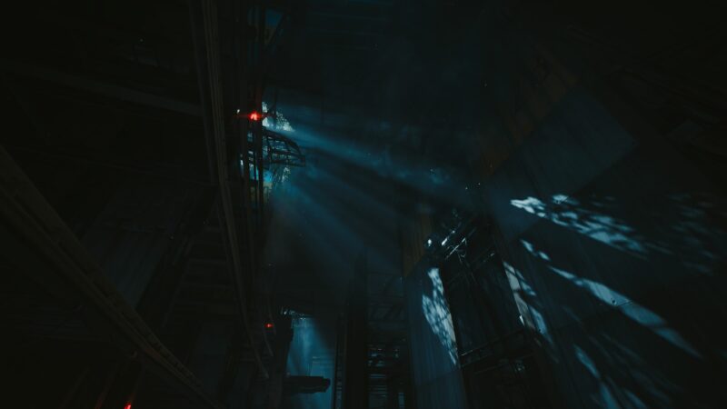 A dimly lit industrial environment features towering structures and beams of light cutting through the darkness, casting intricate shadows on the surfaces below.