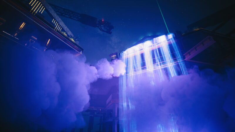 A futuristic building emits bright, vertical beams of light through a misty atmosphere, surrounded by dark structures and a night sky filled with stars.
