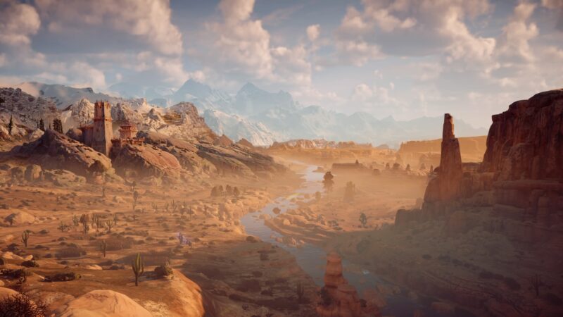 A vast, arid landscape features rocky formations, a winding river, scattered vegetation, and distant snow-capped mountains under a vibrant sky filled with fluffy clouds.