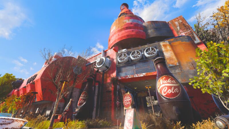 A vibrant, rust-coloured building resembling a giant soda factory features large Nuka-Cola logos, weathered textures, and an overgrown landscape under a clear blue sky.
