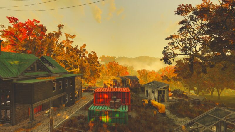 A vibrant autumn landscape featuring dilapidated buildings and colourful containers, set against a backdrop of trees with orange and yellow foliage under a hazy sky.