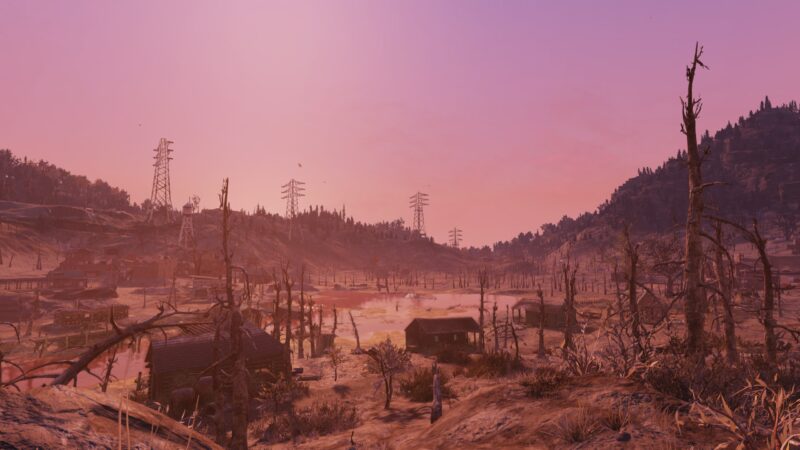 A desolate landscape features barren trees and dilapidated houses surrounding a still, pink-tinted body of water, with distant power lines amidst a fading sunset.