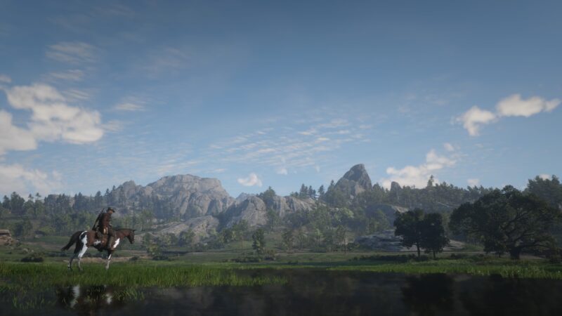 A lone rider on a horse stands by a tranquil body of water, with towering mountains and lush greenery under a clear blue sky, creating a serene landscape.