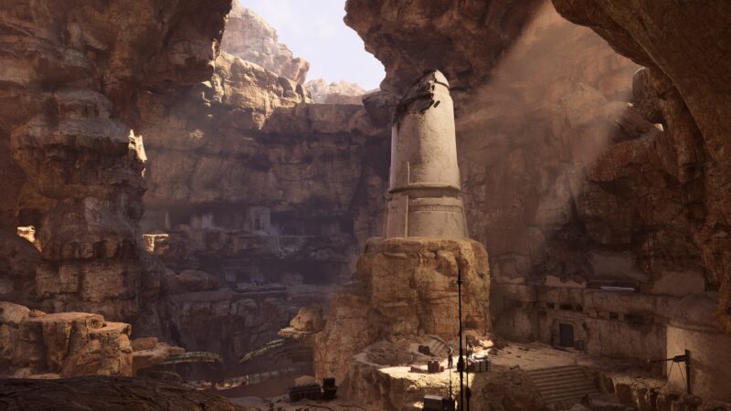 A sunlit cavern features towering rock formations, a central stone monument, and remnants of ancient structures, with warm colours highlighting the rugged terrain and atmospheric dust.
