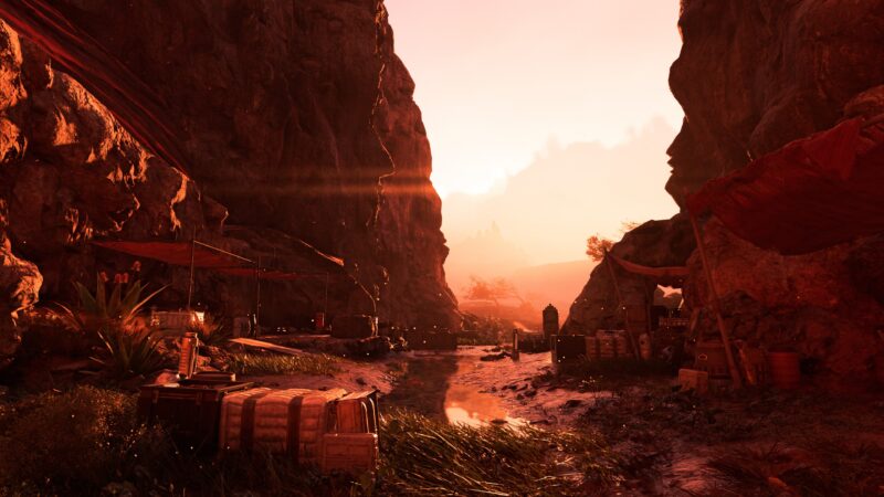 A narrow canyon bathed in a warm sunset glow, featuring scattered wooden crates, tents draped with fabrics, and a reflective waterway amidst rugged cliffs.