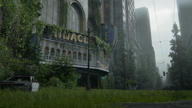 A dilapidated theatre with an overgrown marquee stands amidst a desolate urban landscape, surrounded by tall buildings and dense greenery under a grey, misty sky.