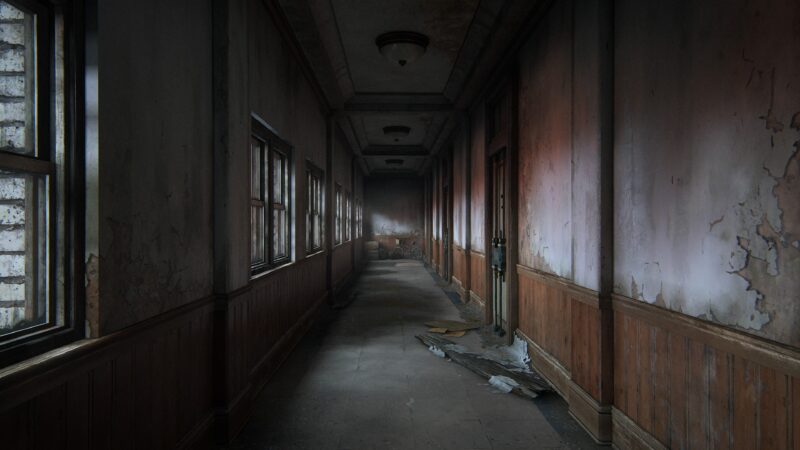 A dimly lit, abandoned hallway with peeling walls and scattered debris, featuring several windows that allow muted light to filter through.