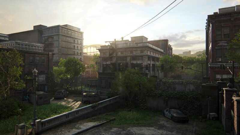 A sunlit, overgrown urban landscape features abandoned buildings, parked vehicles, and scattered greenery, creating a serene yet desolate atmosphere in a post-apocalyptic setting.