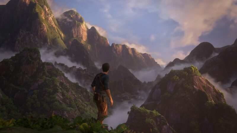 A character stands on a mountain ledge, gazing over lush, mist-covered peaks and valleys under a dramatic sky, with vibrant green foliage in the foreground.