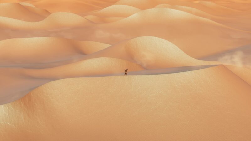 A lone figure walks along a ridge of golden sand dunes, with soft waves and a hazy atmosphere creating a serene desert landscape.