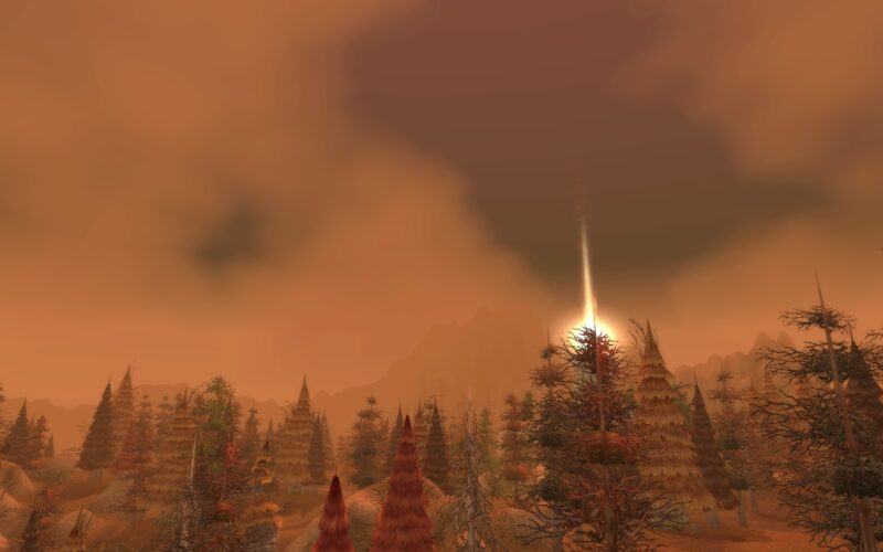 A landscape with a hazy, orange sky at sunset, featuring various types of trees in shades of red and brown, set against distant mountains.