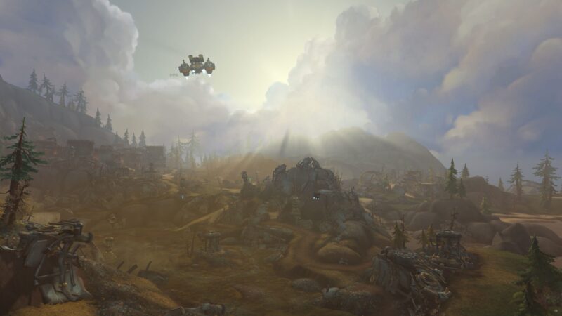 A sprawling, rocky landscape is illuminated by sunlight breaking through clouds, with a distant flying machine hovering above the terrain dotted with trees and remnants of structures.