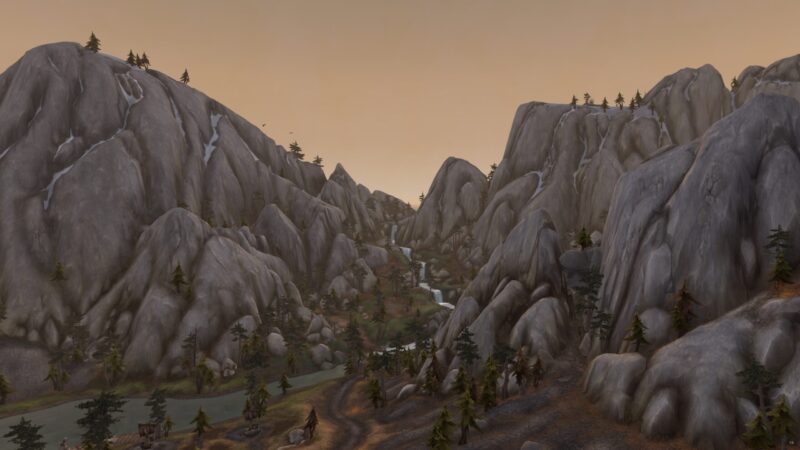 A rugged mountain landscape features towering grey rocks, a winding stream, patches of forest, and a soft orange sky at dusk, creating a serene natural setting.