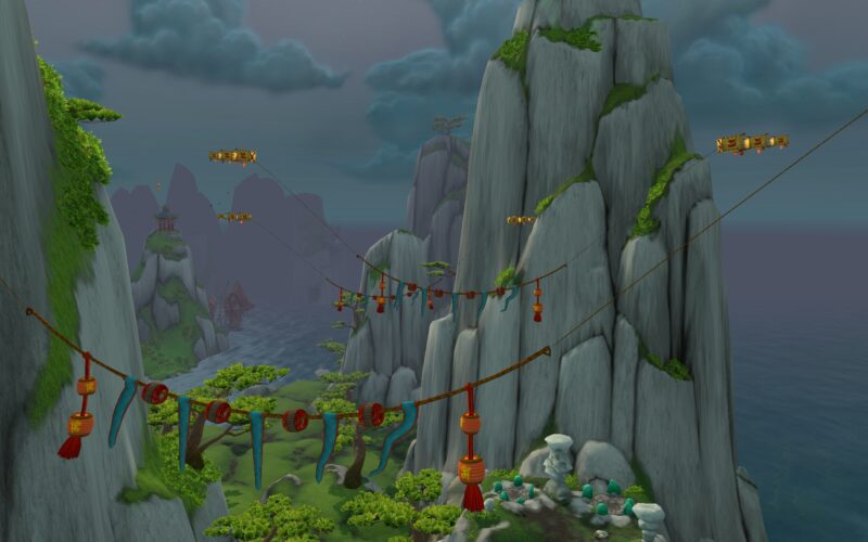 A misty landscape features towering grey mountains, hanging lanterns on cables, and green trees, with a calm ocean visible in the background under a cloudy sky.