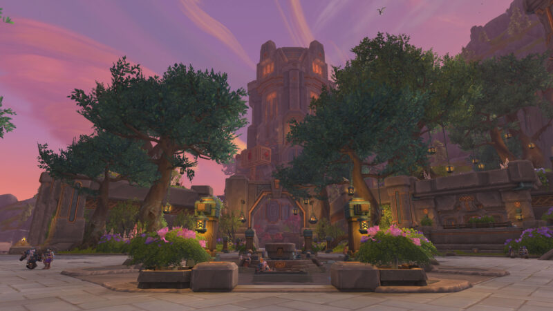 A grand stone structure with turrets rises among lush green trees and vibrant flowers, illuminated by warm lights against a backdrop of a colorful sky at dusk.